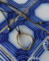 Collar con dije circular irregular de alpaca y plata 925, con hilo de algodón natural.