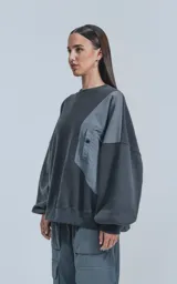 Buzo gris oscuro de cuello redondo, corte oversize y largo crop. Presenta un bolsillo grande de microfibra gris claro en el frente.