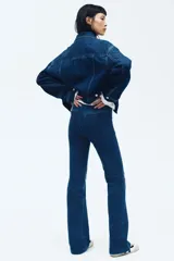 Jean de tiro alto con corte acampanado desde la rodilla. Confeccionado en denim con leve stretch, presenta cierre frontal con botón oculto y corchete, bolsillos traseros decorativos y pliegues frontales y posteriores.