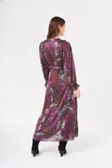 Vestido largo cruzado con estampado floral en tonos fucsia, negro, rojo y blanco. Tiene escote en V con volantes, mangas largas abullonadas y lazo para ajustar en la cintura.