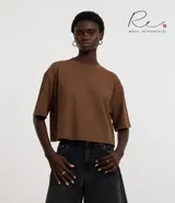 Blusa color beige, cropped y de corte amplio, confeccionada en tejido de media malla, con cuello redondo y mangas cortas.