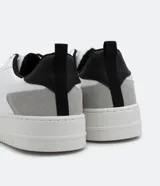 Championes urbanos de cuero sintético blanco con recortes en gris y negro, cierre con cordones y suela de goma.