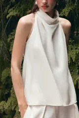 Top blanco satinado con cuello halter y escote fluido. Cierre en la espalda con botones.