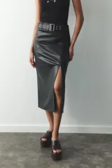 Falda midi negra de cuero sintético, de tiro alto, con cinturón con hebilla metálica y abertura frontal. Cierre lateral con cremallera oculta.