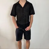 Camisa negra tejida con diseño calado, corte regular, cuello tipo polo y cierre frontal con botones.