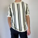 Remera tejida de manga corta con cuello redondo y diseño a rayas verticales en tonos blanco, gris y negro.