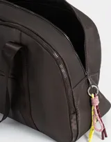 Bolso color beige de tela deportiva con manijas superiores y cierre superior. Tiene un bolsillo frontal con cierre y bolsillos laterales con cierre y tiradores de cordón y goma.