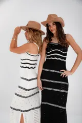 Vestido largo de punto calado blanco con rayas horizontales negras y breteles finos. El vestido tiene un corte recto y aberturas laterales en el ruedo. Las modelos llevan sombrero de estilo cowboy y botas de cuero.