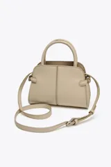 Bolso mini city color beige con doble asa de mano y asa bandolera extraíble. Tiene detalles laterales, pespuntes en el cuerpo y cierre con solapa y botón imantado.