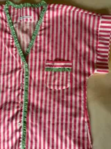 Pijama de algodón estampado a rayas verticales rosas y blancas, compuesto por una camisa de manga corta con botones y volados, y un short con elástico en la cintura.
