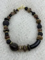 Collar corto con cuentas de piedra volcánica negra, cuentas de madera en tonos marrones y beige, y detalles metálicos dorados.