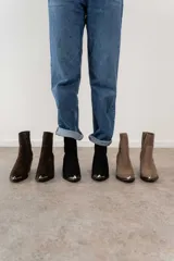 Bota corta de cuero gamuzado color marrón oscuro, con punta fina y detalle metálico. Tiene cierre lateral y taco de madera.