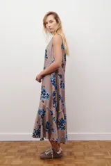 Vestido midi color beige con estampado de hojas en tonos violeta, verde y negro. Diseño sin mangas, con escote redondo y falda acampanada.