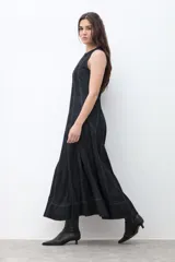 Maxi vestido sin mangas de denim oscuro, con corte al cuerpo en el torso y falda acampanada que cae hasta el tobillo. Presenta costuras visibles en contraste que definen los paneles del vestido.