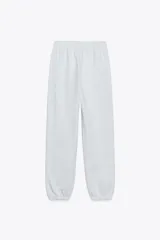 Pantalón de jogging gris claro, de tiro alto, con cintura elástica ajustable con cordones, bolsillos laterales y texto estampado en el frente.
