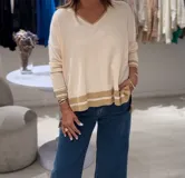 Sweater color crudo con escote en pico, mangas largas y puños con punto elástico en contraste color camel. Presenta abertura en los laterales y la parte trasera es más larga que la delantera.