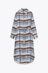 Vestido camisero midi de Zara Woman Collection, confeccionado en ramio 100%. Diseño a cuadros en tonos celeste, marrón y blanco. Cuello solapa, manga larga con puños, cinturón ajustable con lazadas y bajo asimétrico con aberturas laterales. Cierre frontal con botones.