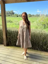 Vestido verde militar de lino, corte a la rodilla, sin mangas, con cuello mao y botones de nácar. Presenta varios cortes en su largo, aportando movimiento y un toque moderno a este diseño fresco y elegante.