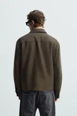 Sobrecamisa negra de lana con cuello solapa, manga larga con puños abotonados, bolsillos de vivo en la cadera y cierre frontal con cremallera.