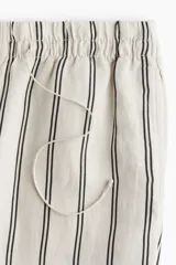 Pantalón de corte holgado en tejido liviano de mezcla de lino. Modelo de tiro alto con cintura elástica y cordón para ajustar fino, bolsillos laterales discretos y piernas rectas. Diseño a rayas verticales en blanco y negro.