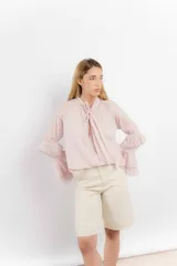 Blusa color rosa pálido de tejido fresco y liviano, con cuello alto con lazo y mangas largas con volados.