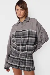 Minifalda gris con estampado de cuadros escoceses, cintura ancha, tablas en la parte inferior y cierre metálico lateral. Incluye sobrefalda desmontable con bolsillo.