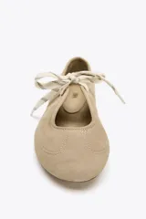 Zapato plano tipo bailarina color beige, de serraje, con puntera redondeada, suela plana y cierre con cordones.