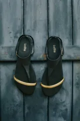 Sandalias planas negras con tira delantera y pulsera al tobillo, detalle de aplique metálico dorado en la puntera.