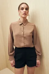 Camisa blanca de manga larga con textura sutil y caída fluida. Presenta cuello clásico, botones forrados a tono y puños con terminación fruncida.