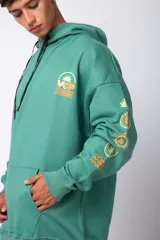 Buzo canguro gris claro de corte oversize, con capucha y cordones negros con letras blancas. Presenta un bolsillo tipo canguro y un estampado pequeño en el pecho y otro en la manga.