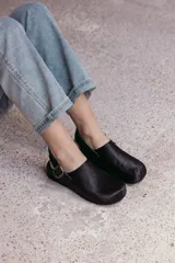 Zuecos negros de cuero con textura de pelo, diseño cerrado con hebilla lateral y tira ajustable en el talón.