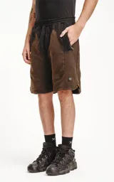 Bermuda de algodón rústico color negro con efecto acid wash/oxidado, corte oversize y cintura elástica. Presenta bolsillos laterales con cierre y un pequeño logo bordado en la parte inferior derecha.