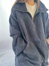 Buzo de pana fina color gris oscuro, con cuello alto y cierre parcial frontal. Presenta un calce holgado y bolsillos delanteros tipo canguro.