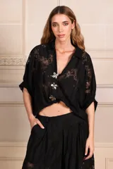 Camisa de encaje negra con escote en V, mangas amplias y cierre frontal con botones adornados con pines florales removibles en plateado y dorado.
