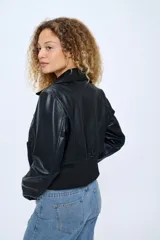 Campera corta de cuero sintético negro, estilo motoquero, con cuello clásico, cierre asimétrico con cremallera, bolsillos laterales con cremallera y puños con cremallera.