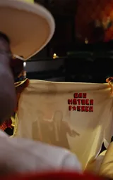 Remera blanca de manga larga superpuesta a una camisa blanca de manga larga, ambas con cuello. La prenda exterior tiene un estampado frontal en naranja con texto censurado inspirado en la película Pulp Fiction.