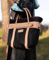 Bolso de playa de lona color verde claro con detalles en cuero color beige. Tiene doble asa de hombro y cierre superior con tira de cuero.