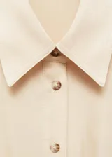 Vestido camisero midi color beige, de tela satinada, con cuello camisero, mangas cortas, dos bolsillos de parche en el pecho, lazo ajustable en la cintura y cierre frontal con botones.