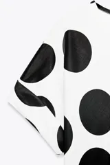 Top blanco con lunares negros grandes, cuello redondo y mangas cortas.