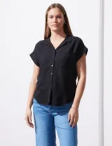 Camisa negra de manga corta con cuello con solapa y abertura central con botones. Delantera con bolsillo aplicado.