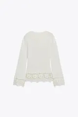 Camiseta blanca de manga larga con cuello redondo y detalle de encaje en el ruedo y puños.