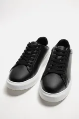 Zapatillas urbanas de cuero sintético negro con cordones y suela blanca de goma con volumen.