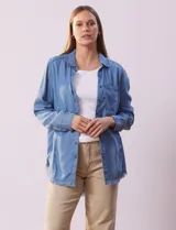 Camisa celeste de tencel marca Hester & Orchand, con cuello con solapa, escote en V y abertura central con botones. Tiene un bolsillo aplicado en la delantera y ruedo desflecado.