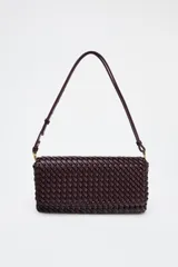 Bolso alargado color borgoña con diseño trenzado, asa bandolera y tirador con pulsera de mano. Incluye bolsillo interior, cierre mediante solapa y botón imantado.