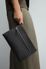 Bolso tipo sobre negro, con compartimento principal con cierre de cremallera, bolsillo interno con cremallera, bolsillo frontal con cremallera y asa de mano.