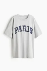 Remera gris de corte amplio con estampado de la palabra "PARIS" en azul.