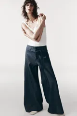 Pantalón de tiro medio azul denim, con trabillas en la cintura y cinturón ajustable con botones. Tiene bolsillos laterales ocultos y pierna ancha.