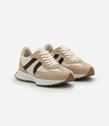 Championes de estilo jogging para mujer, confeccionados en poliuretano color tostado con recortes contrastantes en color crema. Presentan cierre de cordones blancos y suela de PVC que se extiende hasta el talón con base dentada.