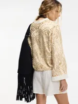 Camisa con estampado geométrico en tonos dorados y negros, con cuello mao y mangas largas acampanadas. Presenta cierre frontal con botones y lazos para atar en la cintura.