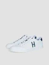 Zapatillas urbanas de corte bajo, color blanco, con cordones y suela de goma. Presentan un gran logo 'H' en color azul marino en el lateral y detalles en azul marino en el talón y la lengüeta.